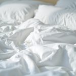 Contrasting clean and slightly stained hostel bedding with rumpled sheets, casting shadows and showing signs of recent use.