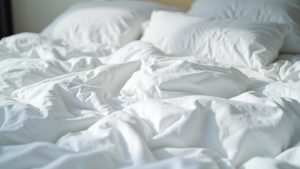 Contrasting clean and slightly stained hostel bedding with rumpled sheets, casting shadows and showing signs of recent use.