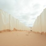 A desert landscape interrupted by translucent synthetic barriers, symbolizing the clash between natural environments and human-made waste.